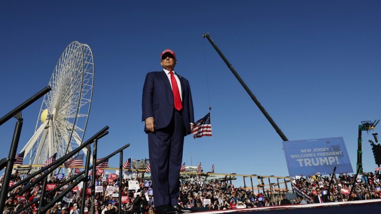 Donald Trump stands on stage at a rally with a giant ferris wheel and crane behind him