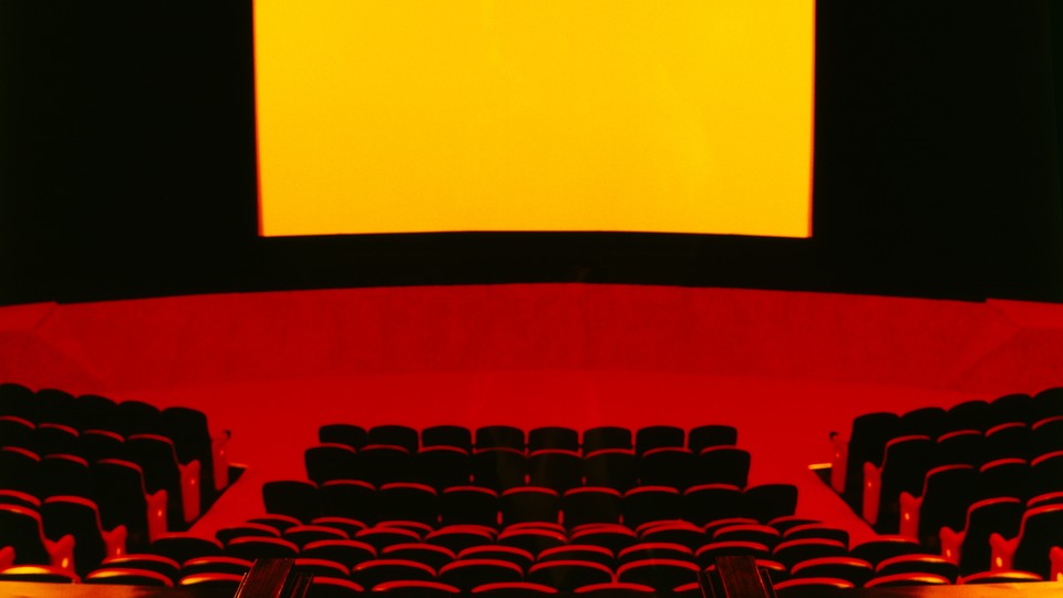 View of movie theater seats and screen, in black, red, and yellow