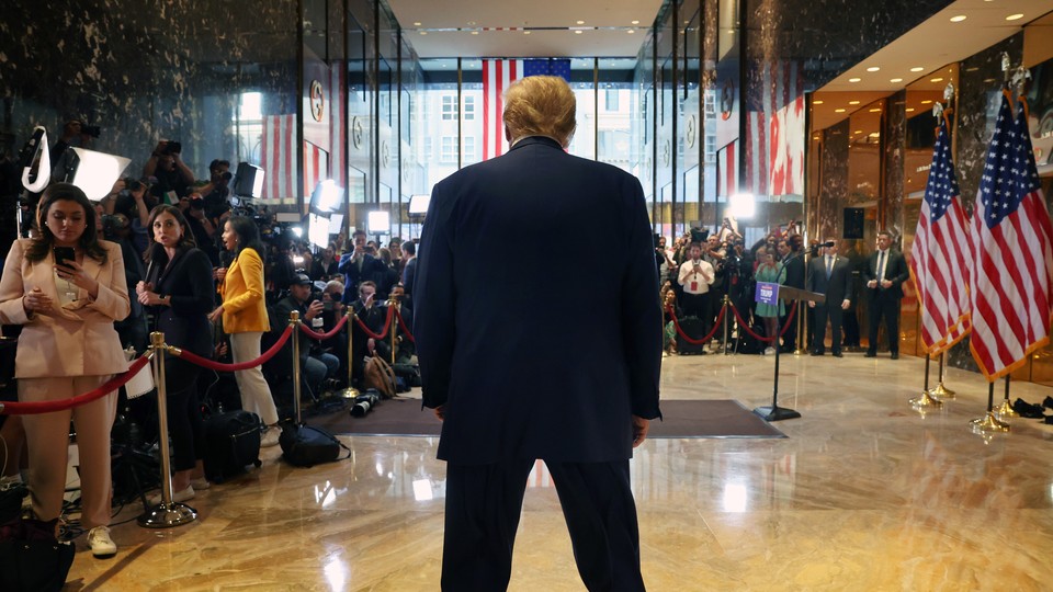 Trump stands, turned from the camera, hunched in front of a crowd of reporters