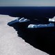 photo of curving white edge of glacier with several calved icebergs and dark blue sea