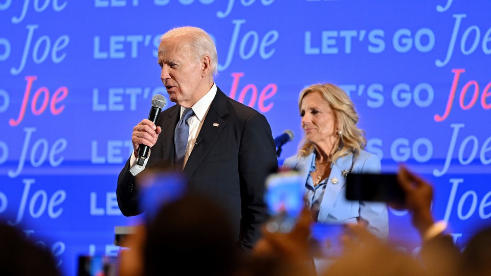 Joe Biden speaking to a crowd, Jill in the back