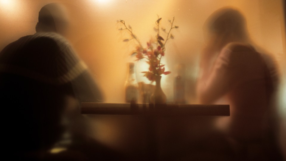 A blurry image of two people seated at a warmly lit table, a vase of flowers between them