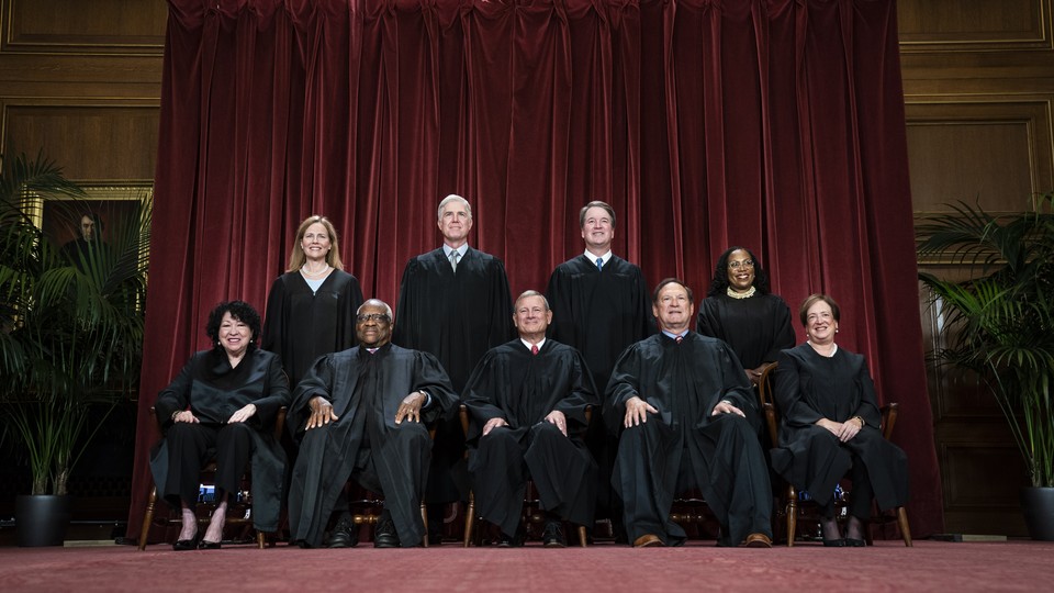 The Supreme Court justices sit in front of a red curtain for a group photo