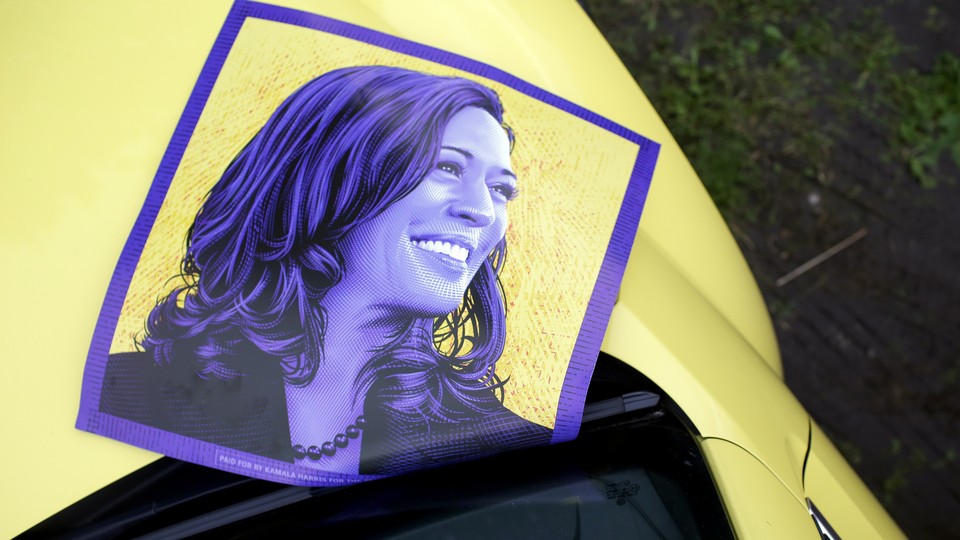 A purple poster of Kamala Harris rests on the hood of a yellow car