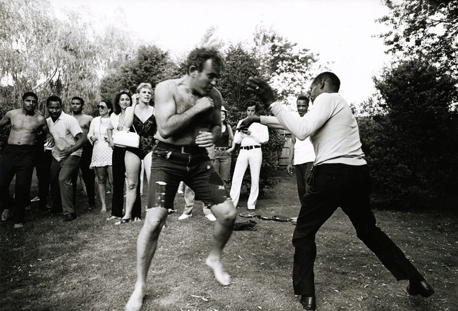 documentary still of Norman Mailer shirtless and boxing an opponent surrounded by a crowd of onlookers