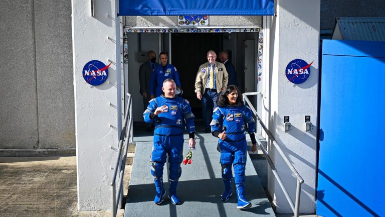 NASA astronauts Barry "Butch" Wilmore and Sunita "Suni" Williams walk out of a NASA building in their blue Boeing spacesuits