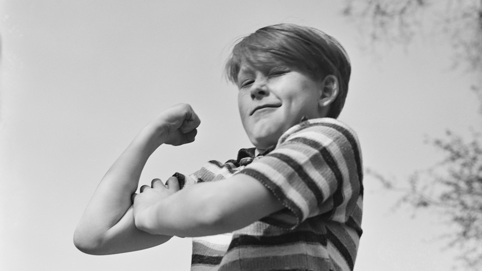 A young boy flexes his arm in a black and white photo