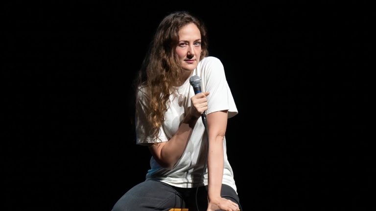 Jacqueline Novak sits on a stool while performing her comedy routine