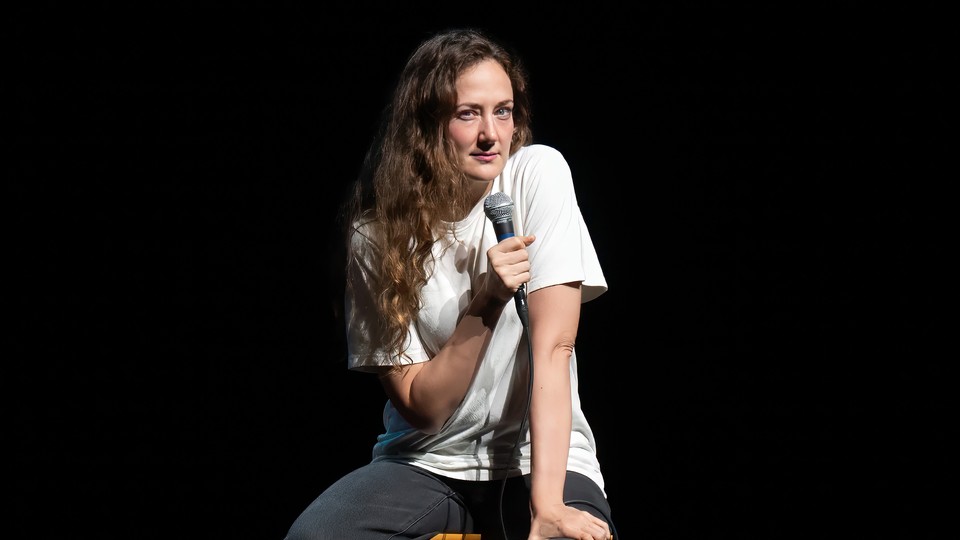 Jacqueline Novak sits on a stool while performing her comedy routine