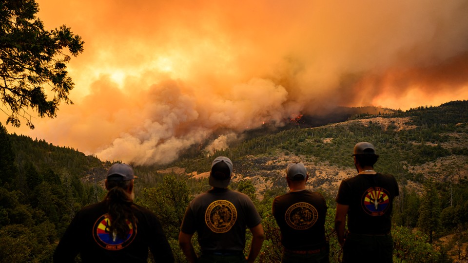 Firefighters watch as flames and smoke move through a valley in the Forest Ranch area of Butte County