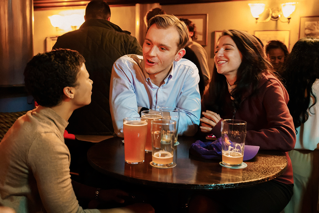 photo of 3 people talking and drinking pints at small round table in pub