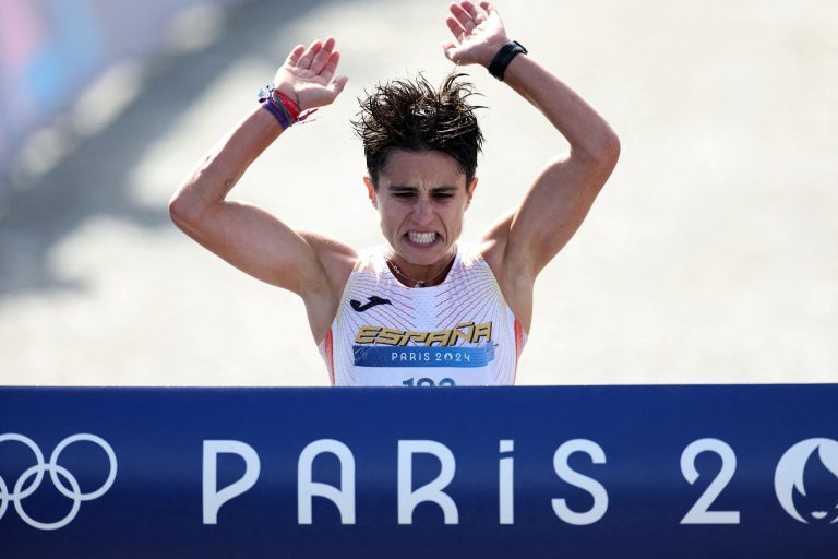 An athlete reacts as they reach the finish line of a race, raising their arms up to grab at the ribbon across the line.