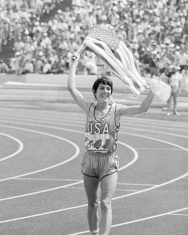 photo of the marathoner Joan Benoit Samuelson jogging while holding up an American flag