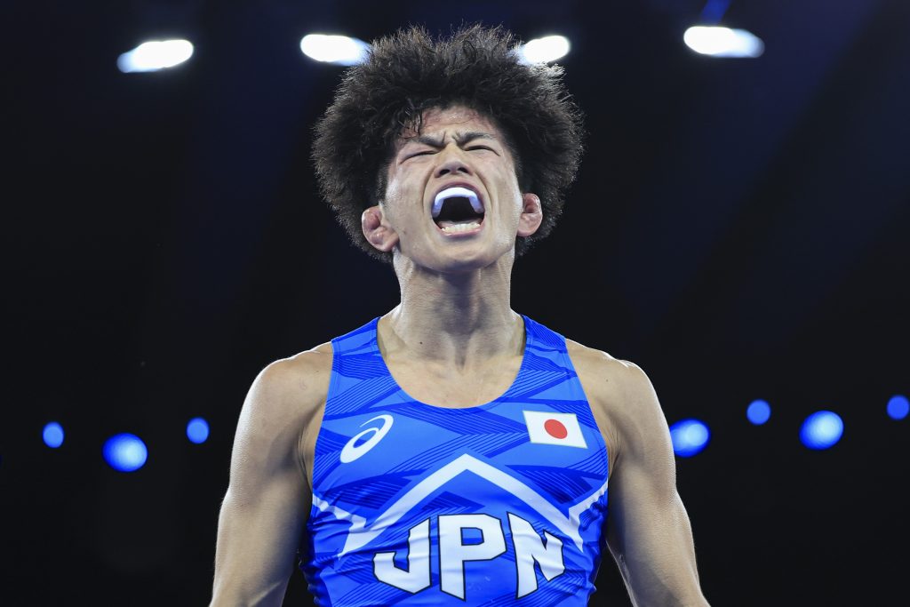 A wrestler celebrates a win, shouting, with his eyes closed.