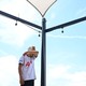 A man wipes his forehead under the hot sun as he walks under shade sail.