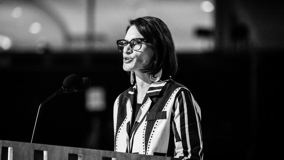 A black-and-white photo of Peggy Flanagan speaking at a podium