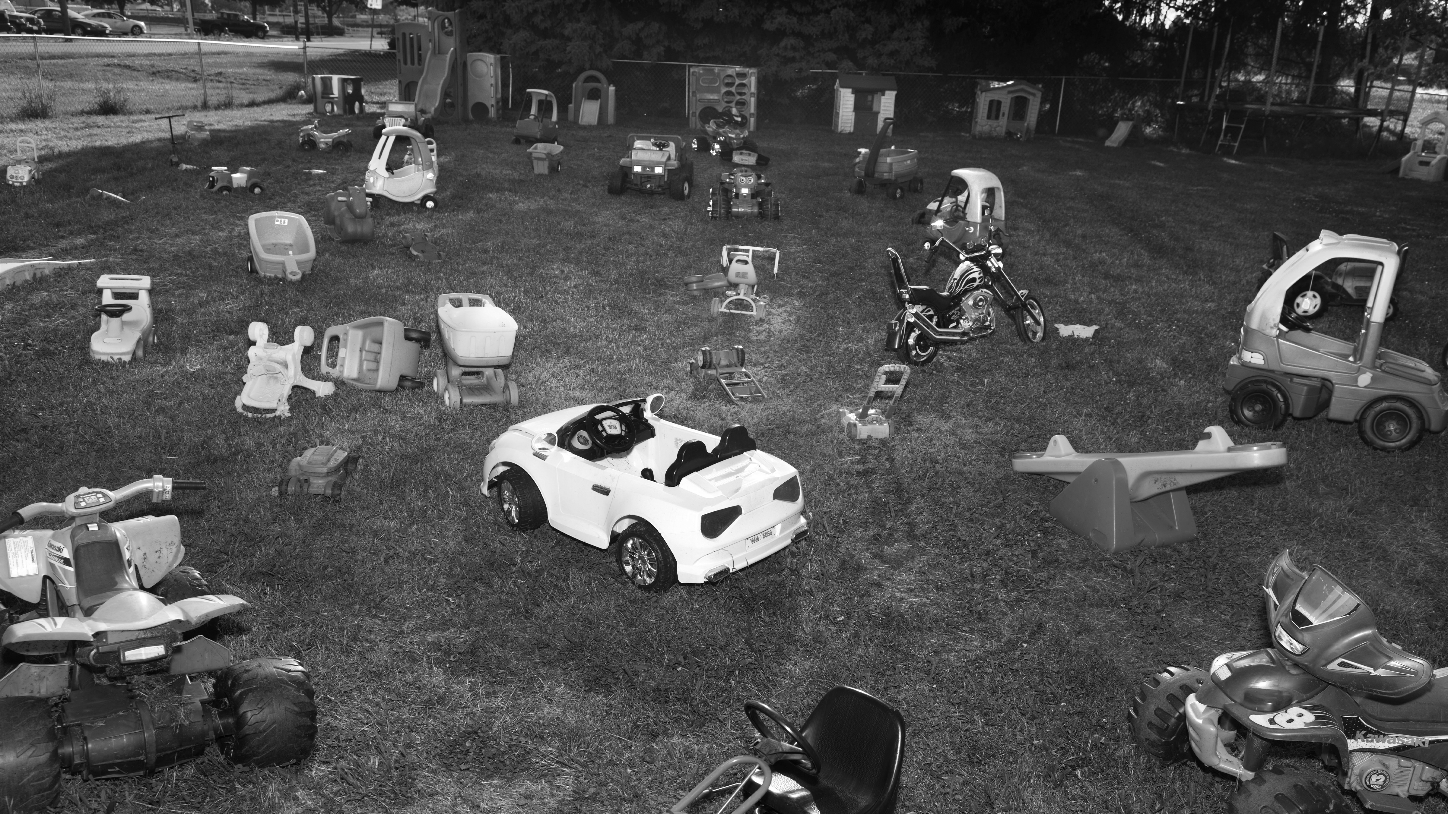 Children's toy cars, mowers, and other equipment strewn across a lawn