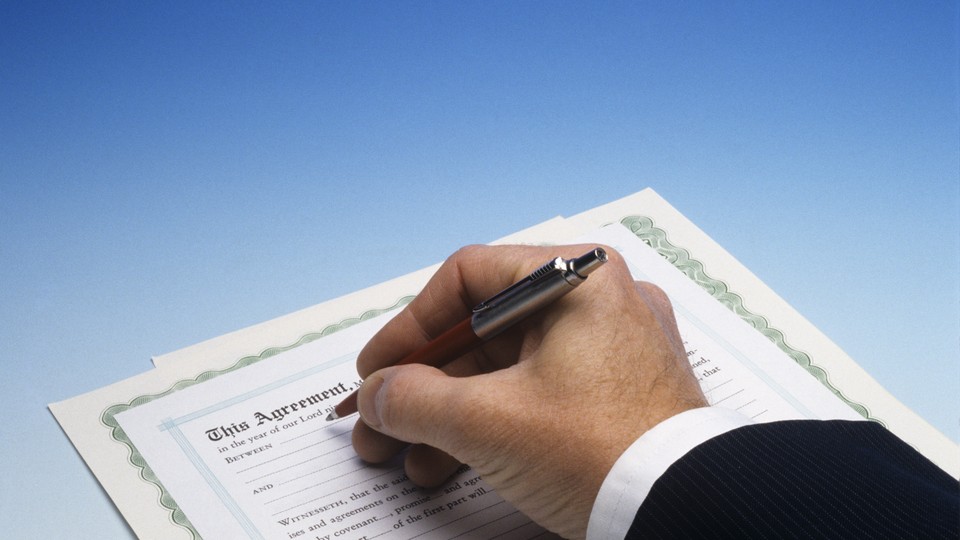 A man wearing a suit signs a contract