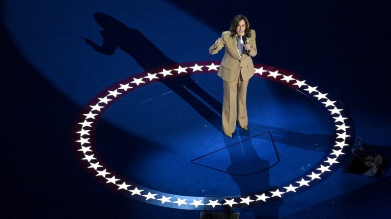 Kamala Harris speaking to microphone, standing in the middle of a circle of stars