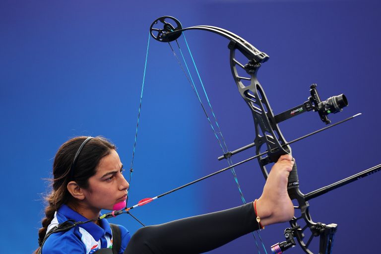 A para-archer draws back an arrow, holding her bow with her right foot.