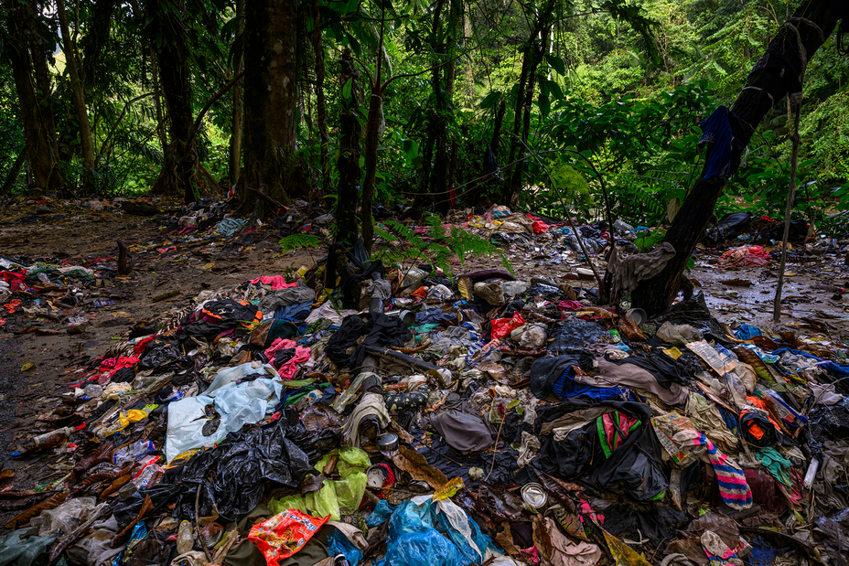 Foto de montones de ropa y suministros esparcidos en el barro con una selva verde de fondo