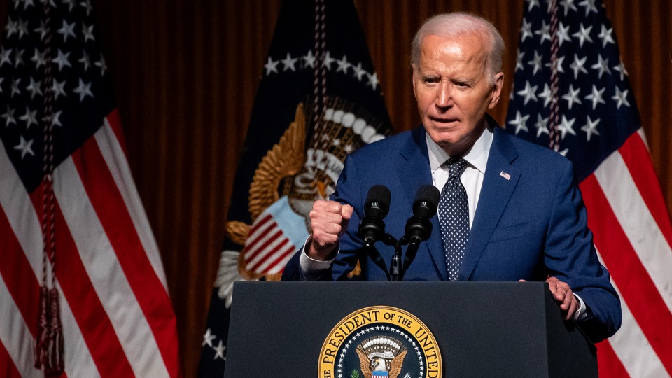 Joe Biden stands at a podium in front of American flags and holds one hand in a fist