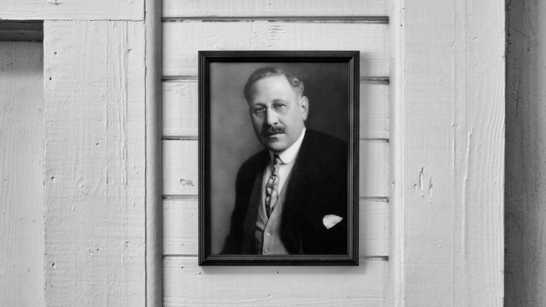 A black-and-white photo of a portrait of a man wearing glasses and a suit.