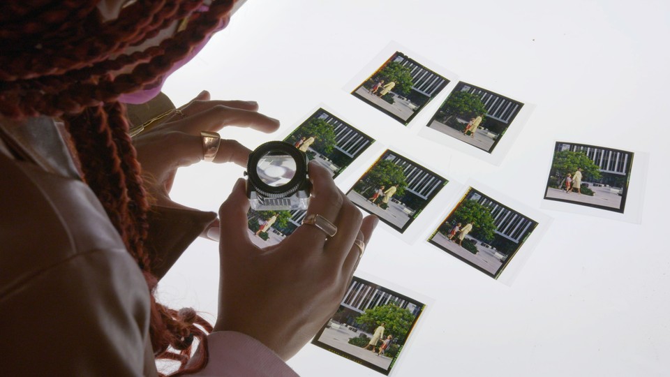 A woman uses a magnifying glass to look at thumbnails from Seeking Mavis Beacon