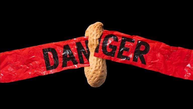 a peanut breaks through red "danger" tape against a black background