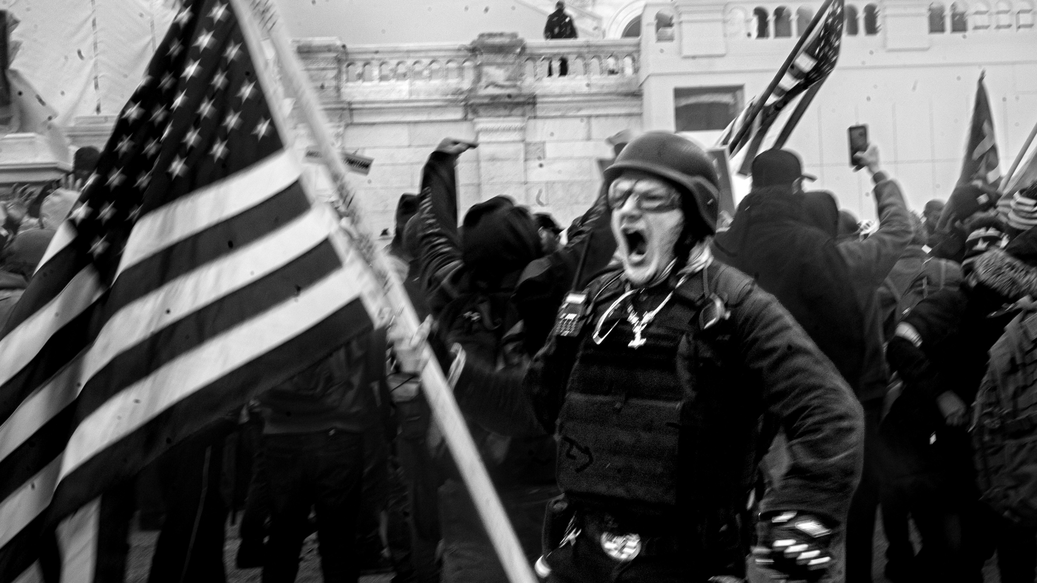 Photo of a man holding an American flag while screaming on January 6, 2021