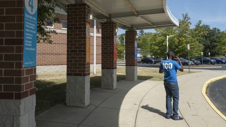 A Haitian father trying to pick up his child speaks on the phone in front of a school