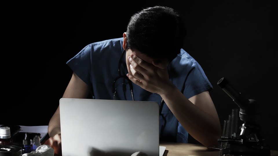 A doctor at a desk with his head in his hands