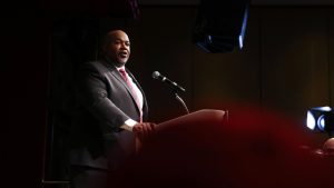 A color photograph of Mark Robinson, in a suit, speaking from a lectern