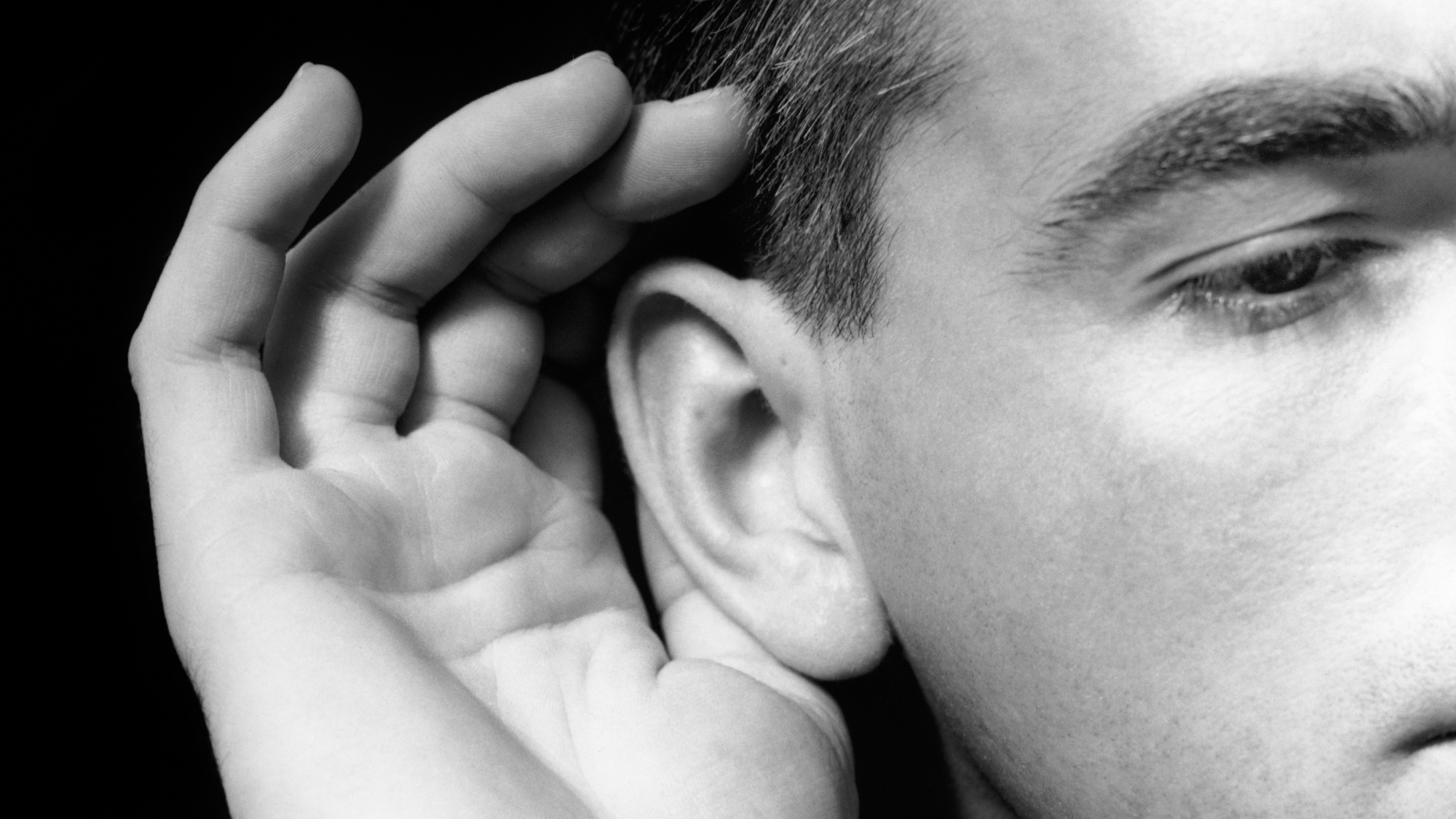 A man cups his hand to his ear