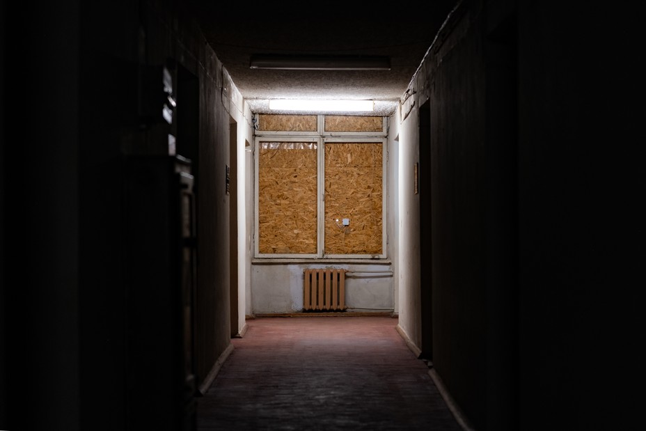 Boarded up window light up by an overhead light at the end of a dark hall way