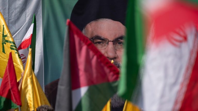 Iranian worshippers wave a Palestinian flag and an Iranian flag in front of a portrait of the Hezbollah leader Hassan Nasrallah.