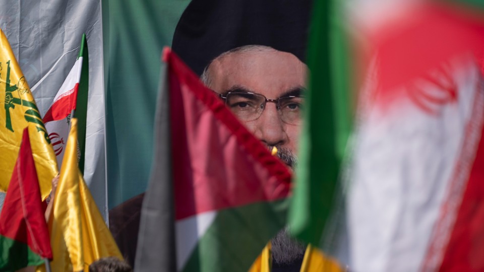 Iranian worshippers wave a Palestinian flag and an Iranian flag in front of a portrait of the Hezbollah leader Hassan Nasrallah.