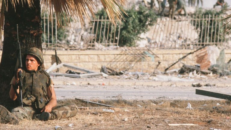 An American sits under a palm tree as his comrades inspect the damage from the suicide bombing that destroyed a Marine barracks in Beirut, Lebanon, in 1983.