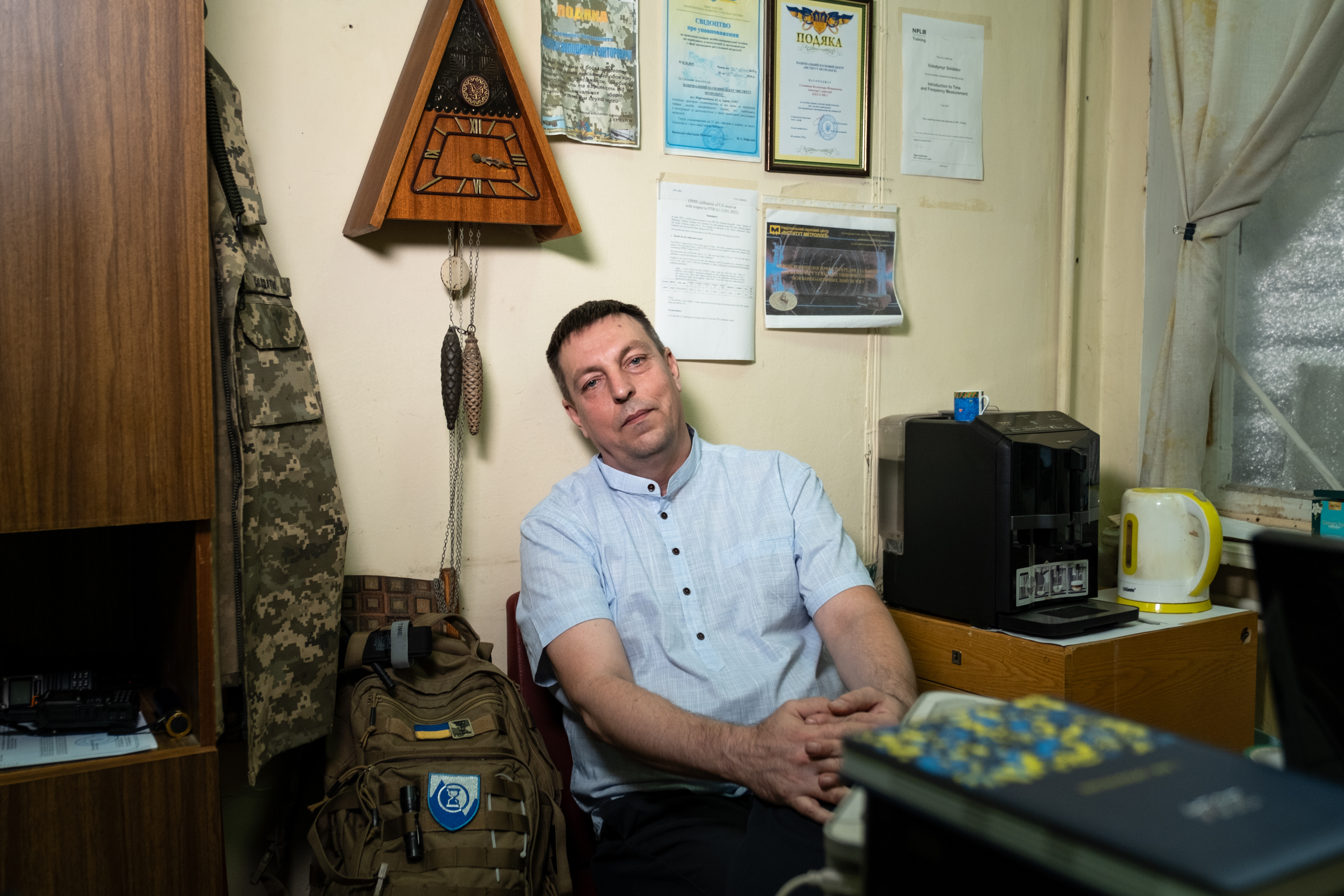 A man wearing a light-blue shirt sits in a chair against the wall in an office.