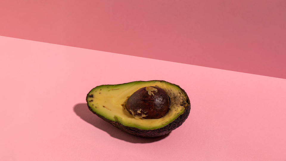 An avocado on a millennial pink background.