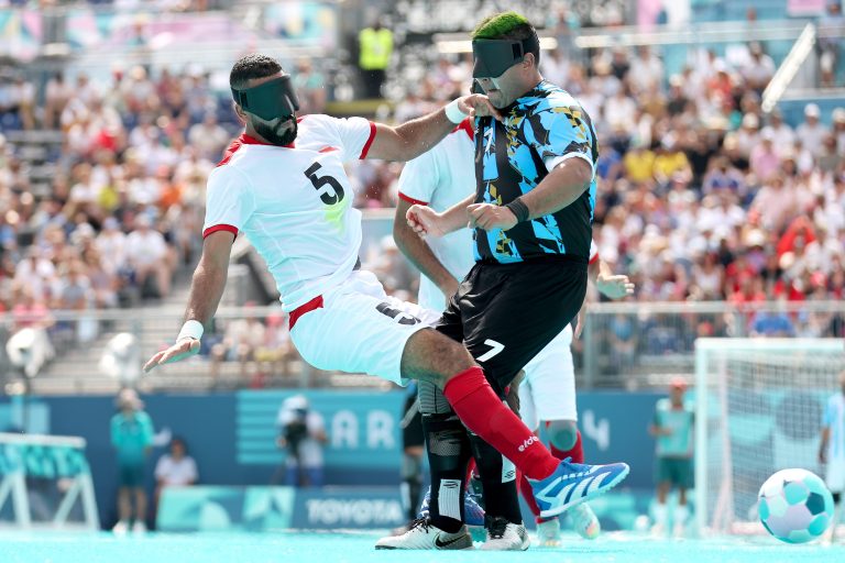 Two football players wearing blindfolds collide while chasing the ball during a match at the Paralympic Games.