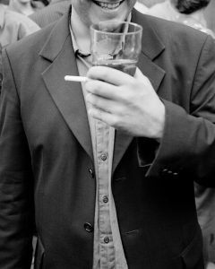 A man smiling with a pint and cigarette in hand.