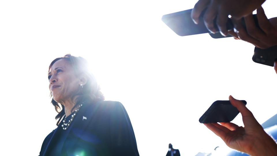 Reporters holding their phones out record Kamala Harris as she speaks to the press