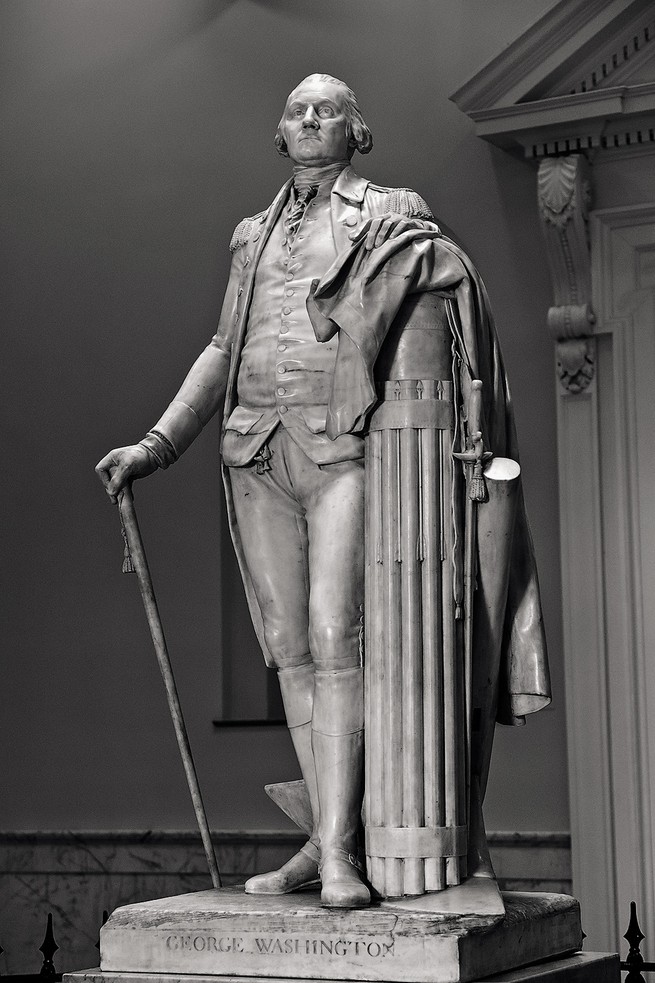 photo of marble sculpture of George Washington standing with one hand resting on military uniform and sword draped over column and the other hand resting on a cane-like stick