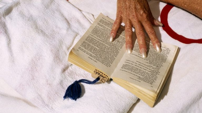 An older person's hand holds a book open on a towel