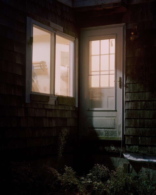 a door and a window to a house revealing a lit interior