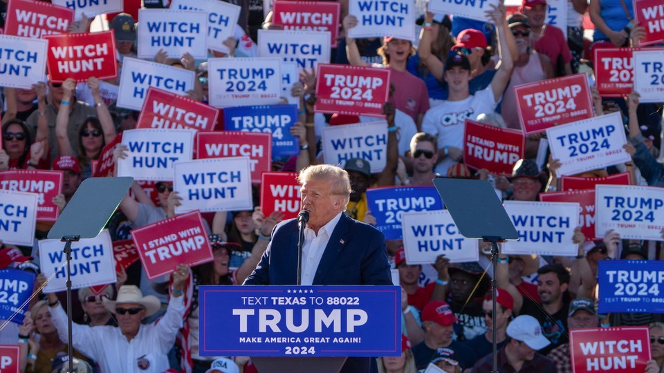 Donald Trump speaks at a rally in front of a sea of signs that say: WITCH HUNT and TRUMP 2024