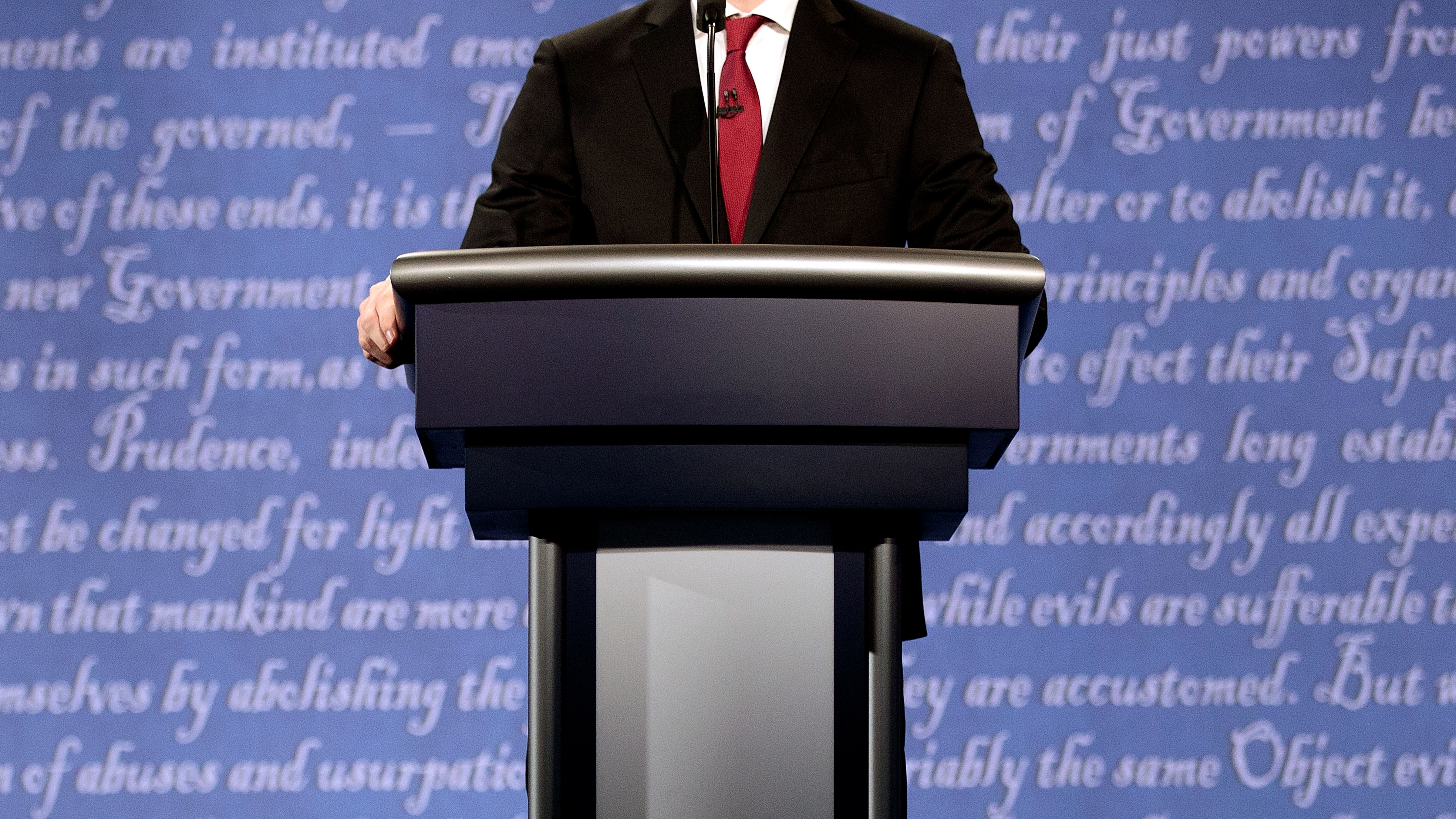 A man stands at a podium in front of a backdrop that quotes the Declaration of Independence