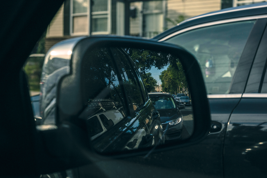 photo of passenger-side mirror and reflection with car and building in background