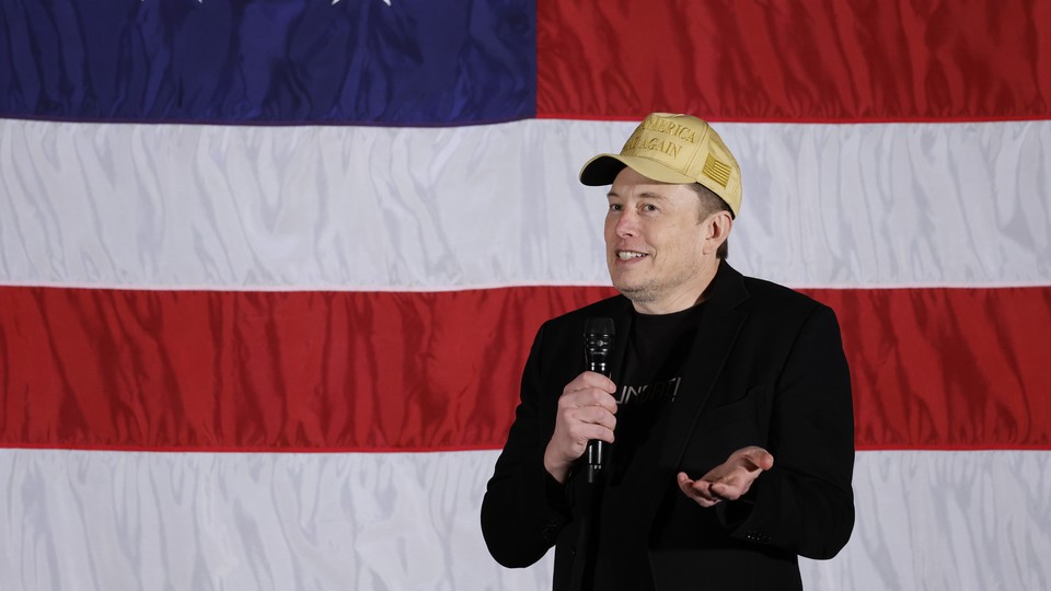 Elon Musk shrugs wearing a MAGA hat in front of an American flag